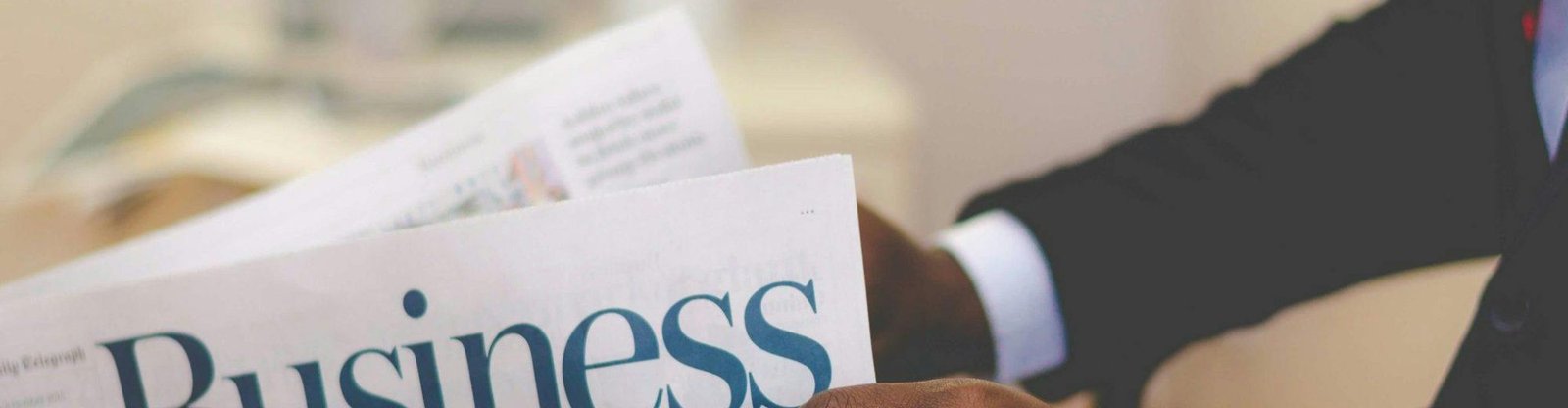 Close-up of a businessman reading a newspaper indoors, focusing on business headlines.