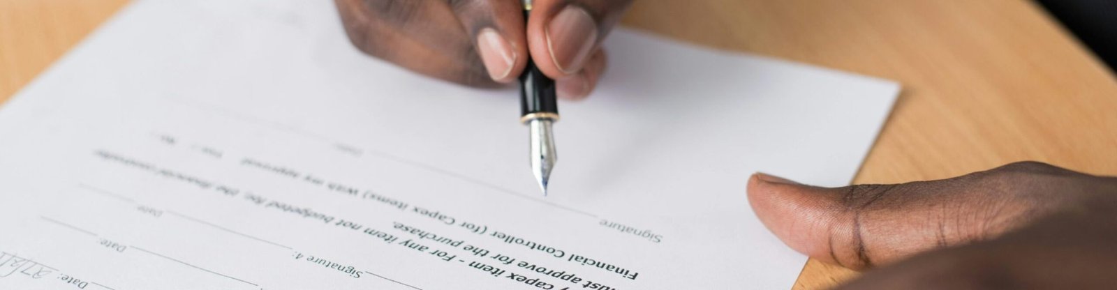 Close-up of a man's hands signing a formal document indoors.